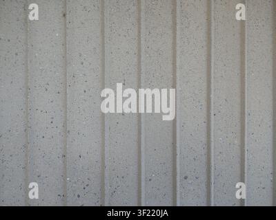 gray concrete wall with vertical relief stripes. The matte, rough surface of the material has small granite inclusions. The strict geometry and rhythm Stock Photo
