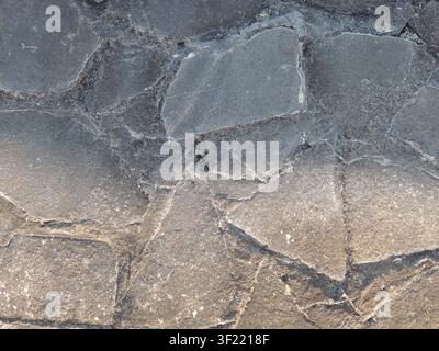close-up of an old pavement made of flat, irregularly shaped gray stones is shown. The large elements are bonded with cement mortar, and cracks, chips Stock Photo