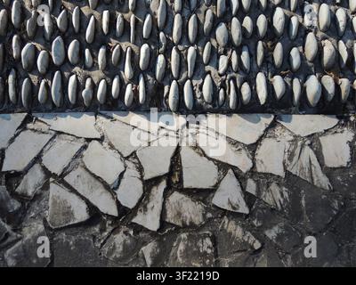 gray stone wall with a rough, textured surface. Beneath it is a sloping slope, densely lined with rows of rounded, light-colored pebbles. Stock Photo