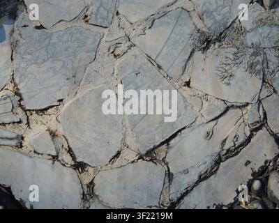 textured stone pavement or wall made of uneven light-gray slabs. Large, flat fragments are joined with light-colored cement mortar. The rough surface Stock Photo