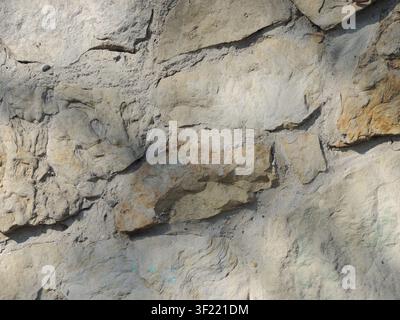 wall of large, uncut, light-colored stones, bonded with cement mortar. The surface has a rough, textured, chipped surface, casting a soft shadow Stock Photo