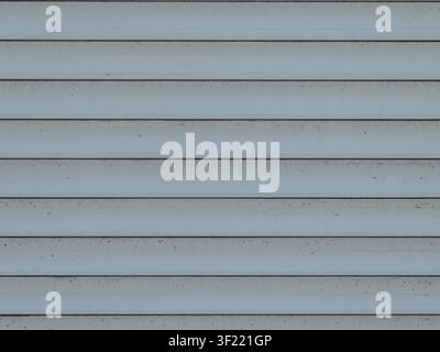 Horizontal plastic or metal siding panels in a light gray color. The surface has a smooth geometric structure with parallel seams and light traces Stock Photo