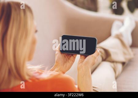 Unrecognizable Woman Holding Smartphone With Blank Screen, Relaxing On Couch At Home Stock Photo