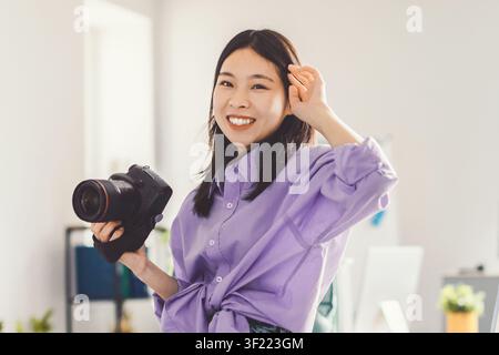 Smiling Asian Woman Holding Camera In Modern Office, Photography Concept Stock Photo