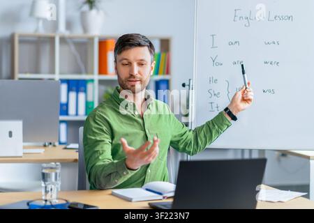 Male Teacher Explaining English Grammar Rules In Classroom, Focused On Lesson Stock Photo