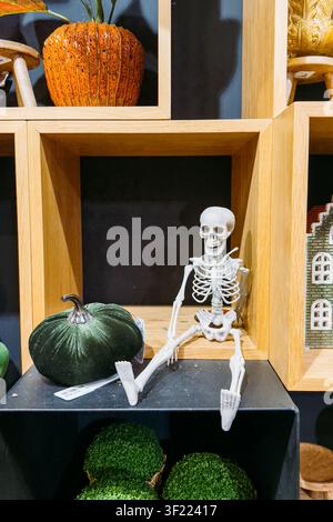 Skeleton figure sits among Halloween decor. Halloween home decor display, minimalist spooky vibe, existential contemplation. Warsaw, Poland -15 July Stock Photo