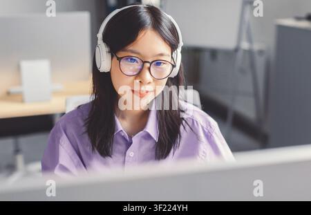 Focused Young Asian Woman Wearing Headphones Working On Computer In Office, Business Concept Stock Photo