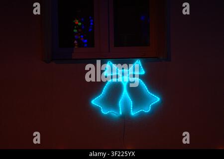 A vibrant and dynamic scene featuring an illuminated neon bell sign mounted on a wall near a window, creating a festive holiday decor atmosphere. The Stock Photo