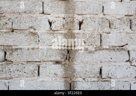 A close up horizontal shot captures the textured detail of an old white brick wall featuring cracked surfaces, visible mortar, and a dark stain runnin Stock Photo