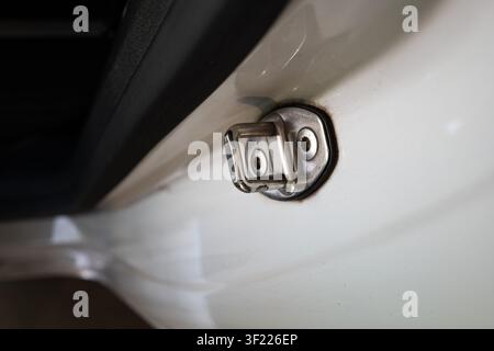 A close up horizontal full shot captures a metallic car door striker plate latch secured with two screws on a clean white vehicle frame. Stock Photo