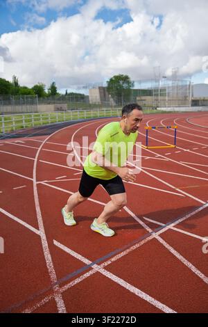 Man in athletic gear and headphones starting a sprint on a running track Stock Photo
