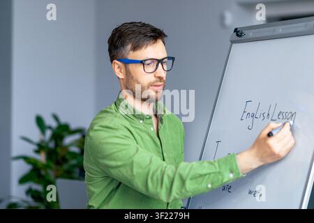 Focused Caucasian Male Teacher Writing English Lesson On Whiteboard In Class, Education Concept Stock Photo