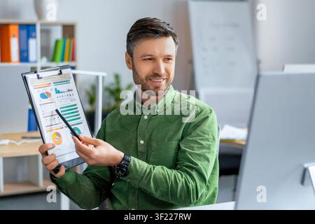 Smiling Caucasian Man Holding Clipboard Presenting Data In Office, Business Concept Stock Photo