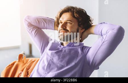 Man Sits Comfortably With Hands Behind Head in Bright Indoor Setting Stock Photo