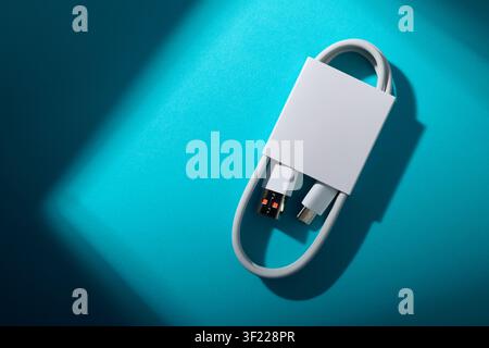 Close-up of a coiled USB-C to USB-A cable from a mobile phone on a green blue surface. These cables are used for fast data transfer and charging of el Stock Photo