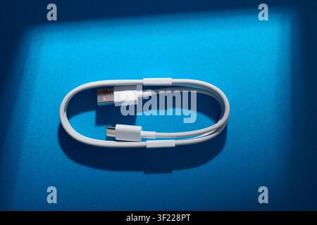 Close-up of a coiled USB-C to USB-A cable from a mobile phone on a blue surface. These cables are used for fast data transfer and charging of electron Stock Photo