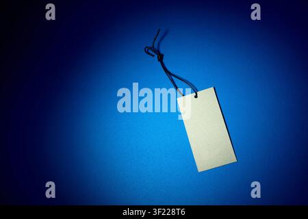 Close-up of a blank cardboard clothing tag on an blue surface. Tag used to indicate the price in retail. Stock Photo