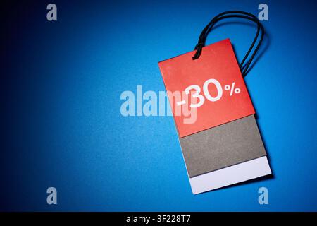Close-up of a blank cardboard tag on a blue surface. Tag used to indicate the retail price and the 30 percent discount. Stock Photo