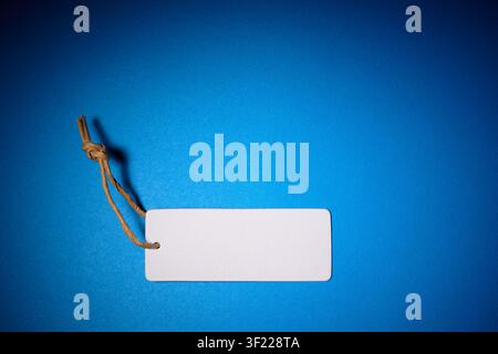 Close-up of a blank cardboard clothing tag on an blue surface. Tag used to indicate the price in retail. Stock Photo