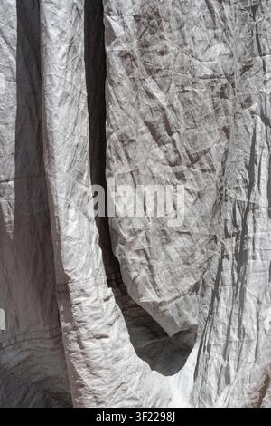 Draped and crumpled grey canvas fabric with deep vertical folds and strong shadows. Stock Photo