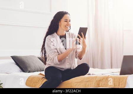 Smiling Young Woman Using Tablet While Sitting On Bed At Home, Relaxation Concept Stock Photo