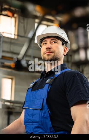 Confident industrial engineer in hard hat standing inside modern manufacturing factory Stock Photo
