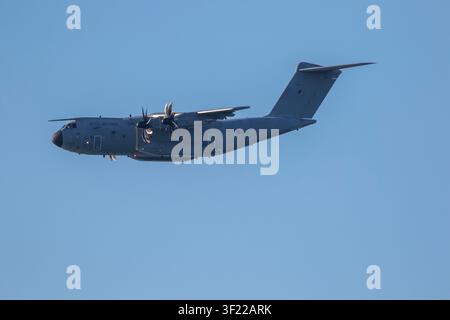 A grey Royal Air Force Airbus A400M Atlas military transport aircraft flying mid-air in banking flight against a clear blue sky background. Stock Photo
