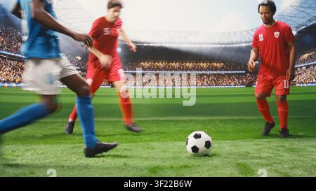 Lower body view of soccer players in red and blue uniforms dribbling each other for ball possession, running across pitch during match play. Footballers in motion blur. Stock Photo