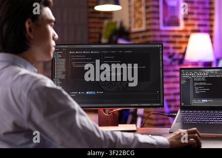 Male remote worker using digital devices in completing programming projects late at night. Asian entrepreneur studying and debugging coding scripts, ensuring functioning website for potential client. Stock Photo