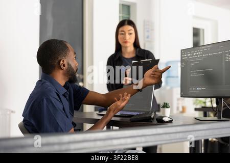 Focused developers work together in a modern startup office, reviewing software information on multiple screens. Team collaboration supports innovation, coding accuracy, and efficient problem solving. Stock Photo
