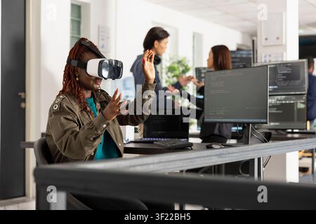 Diverse developers working in modern tech office, featuring female software programmer experiencing augmented reality, pushing boundaries of future technology and metaverse innovation. Stock Photo