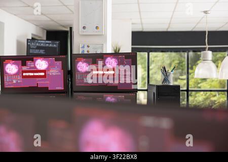Empty office shows multiple computer screens displaying system hacked alerts and warning messages. Cybersecurity breach concept highlights digital risk, network vulnerability and IT security threats. Stock Photo