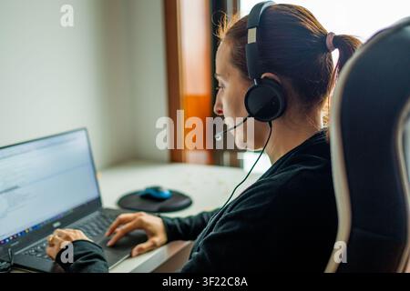 Woman wearing a headset and typing on laptop, providing remote customer service Stock Photo