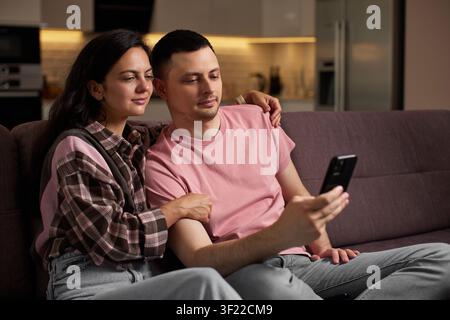 Young couple relaxing on sofa using smartphone Stock Photo