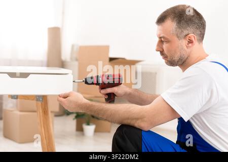 Side-View Of Carpenter Man Assembling Table Using Electric Drill Indoors Stock Photo