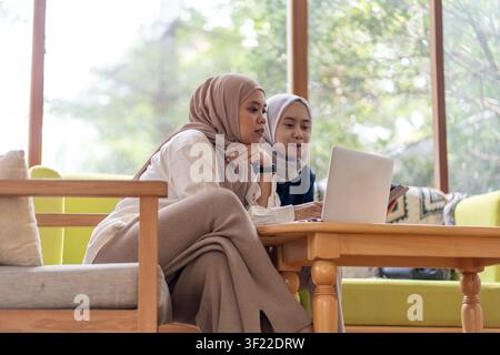Indonesian Muslim professionals working together with digital devices, collaborating remotely in a comfortable modern workspace. Stock Photo
