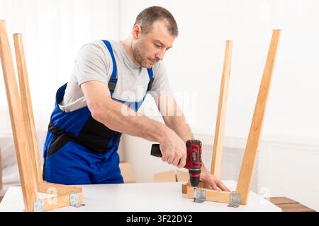 Male Carpenter Using Electric Drill Assembling Wooden Table In Studio Stock Photo