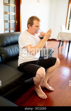 Man managing asthma at home, using an inhaler and spacer for respiratory health Stock Photo
