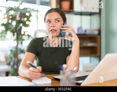 Young woman talking on mobile sitting at office desk Stock Photo