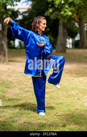 Woman performing a tai chi pose in a park, focusing on balance and concentration Stock Photo