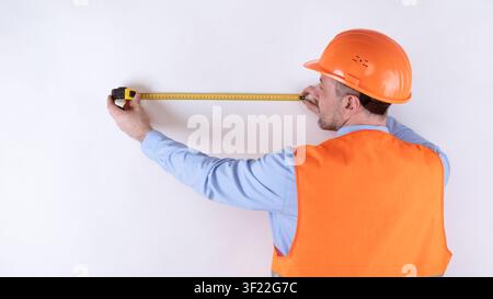 Builder Measuring Wall With Tape-Measure Standing Back To Camera, Studio Stock Photo