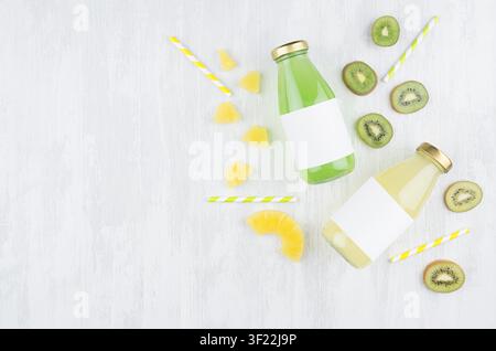 Fresh yellow pineapple juice and green kiwi juice in glass bottles with blank label, ingredients on white wood board, mock up for design, advertising, branding product. Stock Photo