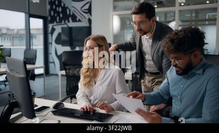 Three joyful multiethnic business people team comparing data stats in documents typing laptop talking happy smiling Caucasian woman businesswoman with Stock Photo
