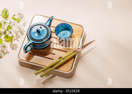 Blue ceramic teapot with blooming spring branch on wooden tray in minimal asian style composition Stock Photo