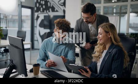 Three multiethnic business office colleagues working together discussing work online papers data talking businessmen males with businesswoman female Stock Photo