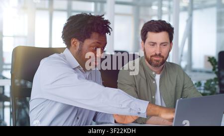 Two diversity businessmen partners looking in laptop together discuss online work multiethnic business men males managers at working conference Stock Photo