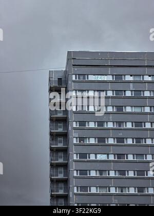 Tall grey residential high-rise against dark overcast sky. Dramatic low angle view of Soviet-era apartment building. Stock Photo