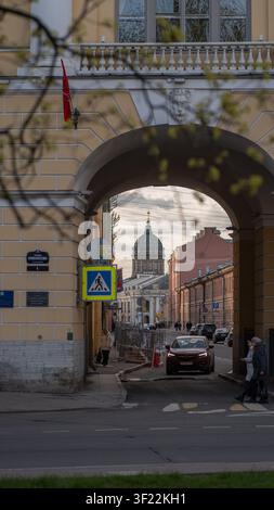 View through historic stone archway to a street with green-domed church. Spring leaves and people in urban classic architecture scene. Stock Photo
