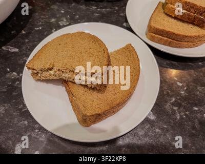Wholemeal bread and butter rounds on white plates sitting on marble effect kitchen counter top. Stock Photo