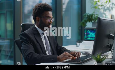 African American business man working typing computer keyboard looking at screen monitor browsing technology at office table. Ethnic businessman male Stock Photo